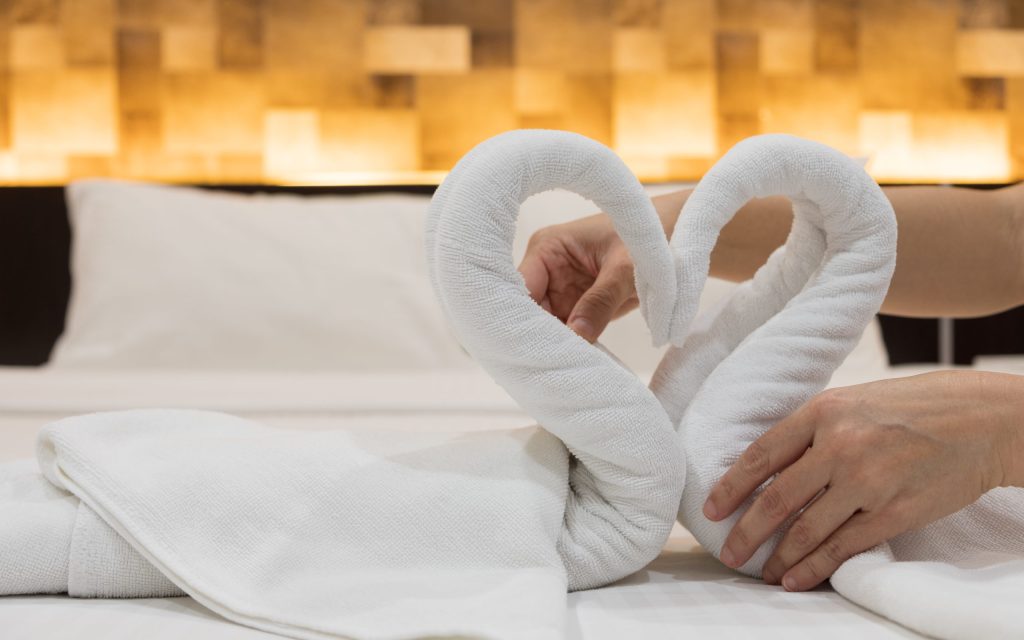 Close-up of hands putting folded swans bird of fresh white bath towels on the bed sheet in the hotel.